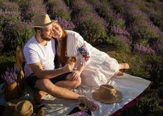 Man and woman hold glasses with white wine on background of a lavender field. Romantic picnic in...