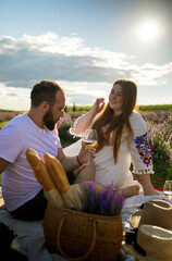 Man and woman hold glasses with white wine on background of a lavender field. Romantic picnic in sunset. 