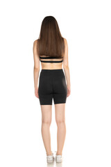 Young woman in black shorts and top posing in the studio on white background. Back view