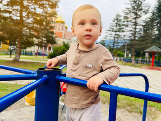 Fototapeta na wymiar A cute boy of one and a half years rides on a swing in the playground. Children's entertainment. Selective focus