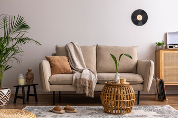 The stylish composition of living room interior with beige sofa with carpet, pillow, plaid, coffee table and personal accessories. Beige wall. Home decor. Tem