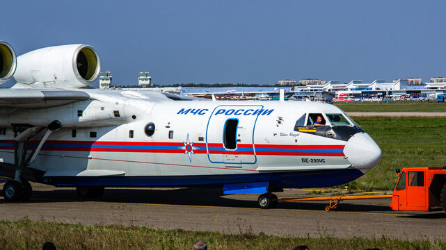 Towing by a tractor of Russian amphibious aircraft (flying boat) - Be-200 "Altair" on taxiway. Close-up. Orange tractor. Blurred background. Selective focus. Zhukovsky, Russia - August 16, 2011