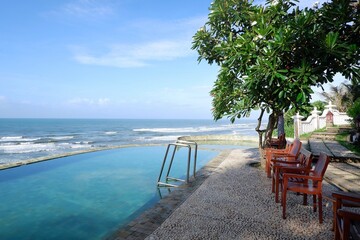 Fresh cool blue pool and ocean waves with infinity view of clear sky background with stairs pool ,wooden chair tree leaves in Parang Tritis beach Yogyakarta, Indonesia