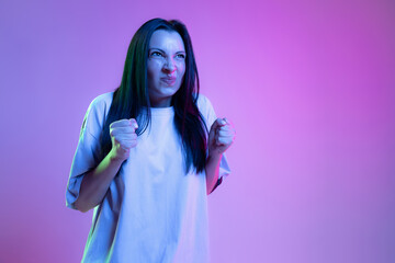 Angry, annoyed girl, young woman with long glossy dark hair isolated on purple background in neon light. Concept of beauty, art, fashion, emotions
