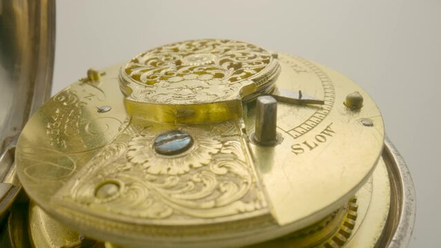 Clockwork mechanism with rotating spring, gears, gearing and toothed wheels. Round wheel with a carved pattern from curlicue on an antique gold clock. Old clockwork on white background. Extra close up