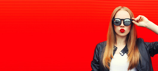 Portrait of blonde young woman blowing her lips with lipstick sending air kiss wearing sunglasses...