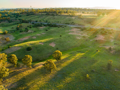 Rays of sunlight over green paddock beside train line