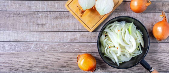 White onion slices in pan for cooking and fresh white onion on gray background.Top view
