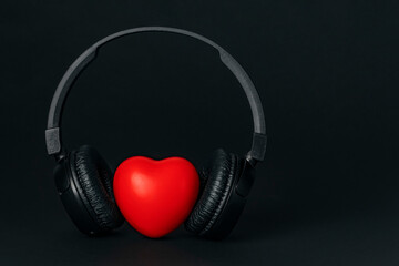 Fototapeta na wymiar Black wireless headphones with red heart on black background. Listen to your heart music of love. Copy space.