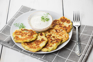 Zucchini pancakes with cream sauce on plate. Healthy diet food. Dinner table setting.