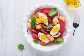 Tuscan Panzanella salad. Fresh tomatoes salad with basil leaves, eggs, olive oil and onion in white bowl on light background. Vegetarian panzanella salad. Mediterranean healthy food. Top view.