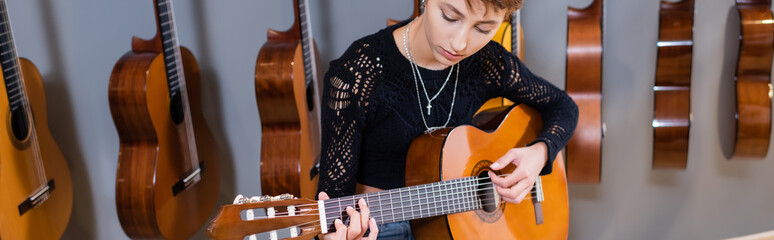 Young woman playing acoustic guitar in music shop, banner.