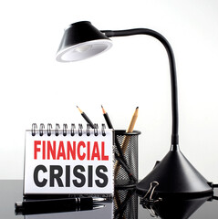 FINANCIAL CRISIS text on notebook with pen and table lamp on the black background