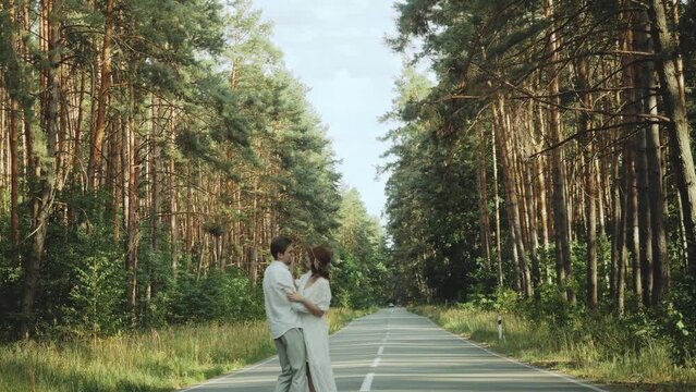 Hipster couple in love walk in beautiful place, hold hands, man and woman hugging and enjoying togetherness on empty road across picturesque pine forest. slow motion 