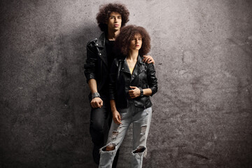 Obraz na płótnie Canvas Young man and woman with leather jackets and curly hair leaning on a dark background