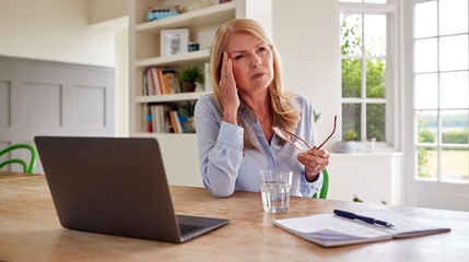 Menopausal Mature Woman Working On Laptop At Home Suffering With Headache Pain