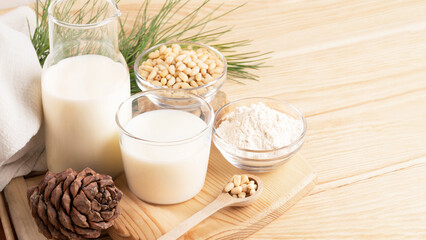 Cedar milk, flour, nuts in glass tableware, cone, branch on wooden table. Banner. Copy space.