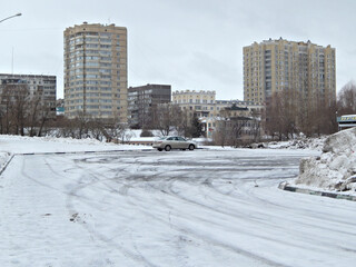 Several tall buildings and a car in a snow-filled parking lot.