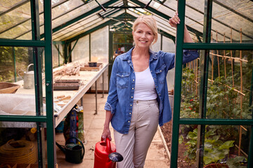 Portrait Of Mature Woman With Watering Can Gardening In Greenhouse At Home