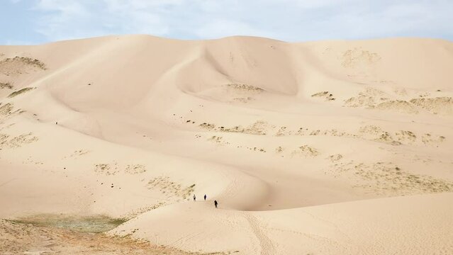 Aerial dolly of three people walking on sand dune in gobi desert in daytime