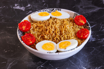 A bowl of noodles with boiled eggs  and cherry tomato.