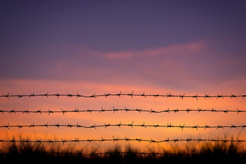 Sunrise behind a wooden barbed wire fence over natural prairie grasslands.