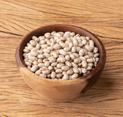 Raw brown beans in a wooden bowl over wooden table