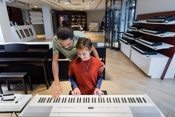 Smiling multiethnic couple playing synthesizer together in music store.