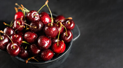 Fresh sweet cherries with water drops in bowl on dark rock table. Copy space. Food background