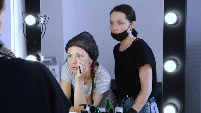 females in a beauty salon discussing eyebrow procedures looking in mirror with light bulbs