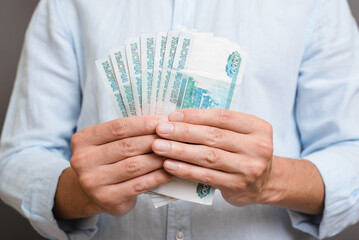 Unrecognizable man in blue shirt holding money russian rubles thousand banknotes indoors. Finance...