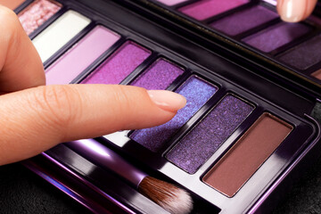 Female finger touching colorful eye shadow palette. Makeup with matte and shimmer shadows by fingers