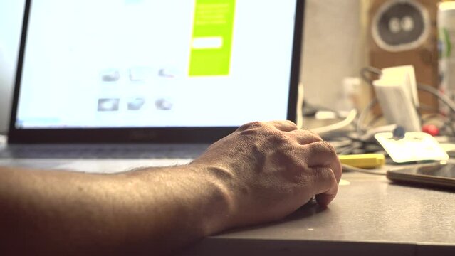 A man watches content on a computer screen. Laptop on the table. Receiving the information. Photo and video content.. Surfing on the Internet. Tester. User. IT-specialist. Close-up.