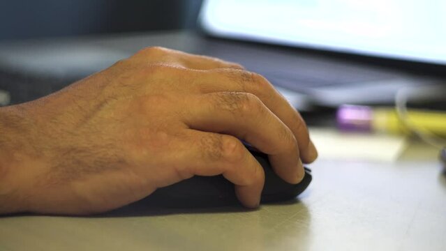 A man's hand holds a computer mouse. Laptop on the table. Receiving the information. Photo and video content.. Surfing on the Internet. Tester. User. IT-specialist. Close-up.