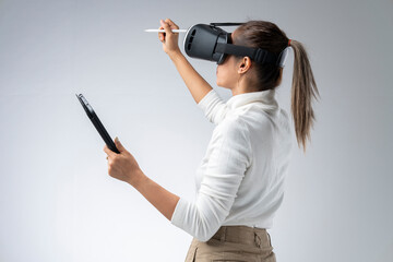 White shirt woman wearing VR glasses holding tablet and pen gesturing in the virtual world.