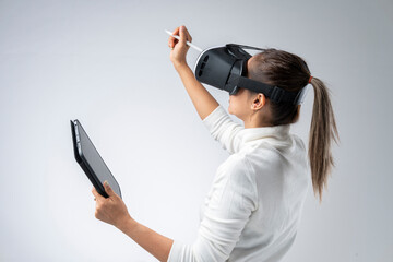 White shirt woman wearing VR glasses holding tablet and pen gesturing in the virtual world.