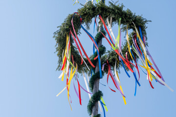 Maypole with wreath with ribbons in Germany against a sky with clouds