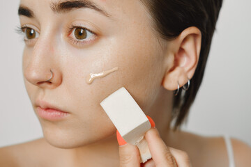 Cosmetics for acne, a woman girl applies a tonal foundation with a sponge to hide problems with the skin of the face, correct the coverage, hide wrinkles.