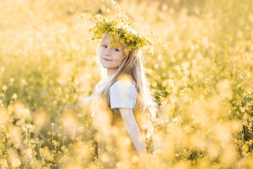 Cute stylish child girl 4-5 year old wear floral wreath stand in yellow flower meadow outdoor over...