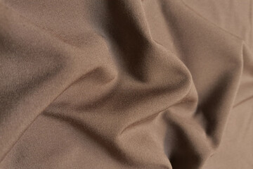 Beige or brown crumpled or wavy fabric texture background. Abstract linen cloth soft waves. Silk atlas or stretch jacquard. Smooth elegant luxury cloth texture. Concept for banner or advertisement.