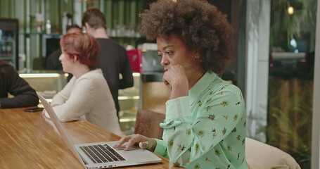 A happy black woman using laptop at coffee shop. One African American girl typing on computer keyboard smiling. A female entrepreneur person looking at laptop screen