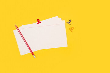 Tarjeta de indice  junto a un lápiz rojo y clips sobre un fondo amarillo brillante liso y aislado....