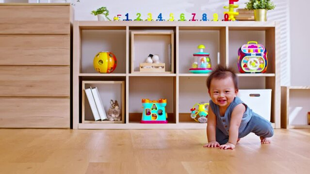 Healthy asian baby toddler crawling on floor to learn to crawl indoors. Adorable baby keeping her belly and legs down on the floor to belly crawl fun and happiness at home. Nursery room