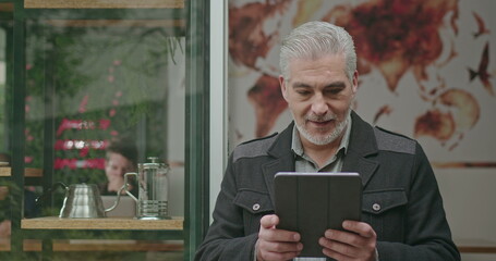 Confident entrepreneur holding tablet in front of cafe store. Portrait of a happy coffee shop owner looking at results smiling feeling confidence. Small business restaurant bar local owner