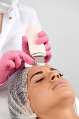 Cosmetologist, beautician in pink gloves making facial treatment with ultrasonic spatula to woman,...