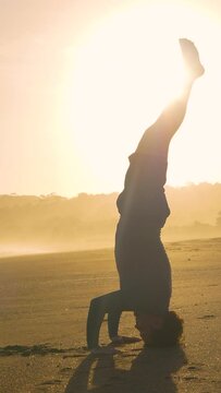 STILL SHOT: Vital young man practising yoga headstand on exotic beach at sunset. Healthy lifestyle during summer holidays in Panama. Yoga workout in golden light on a beautiful shore.