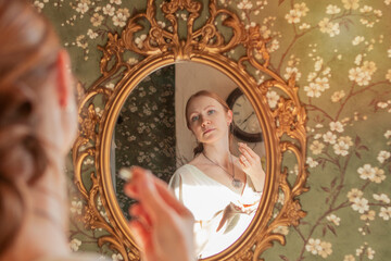 a young girl in a long white dress is scented with perfume in front of a mirror