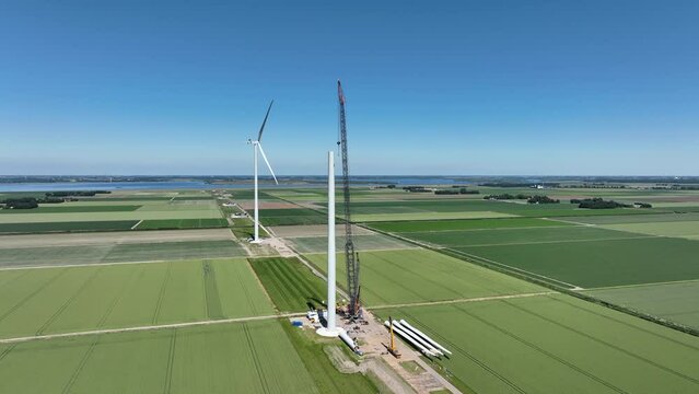 Wind turbine construction with huge cranes at a new wind park in Flevoland, Netherlands. Aerial view drone footage from above.