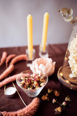 Still life with a bowl filled with small dried roses and several candles..