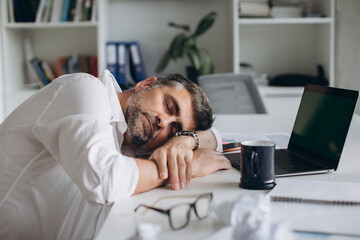 Tired businessman falling asleep during work with documents and laptop in office.
